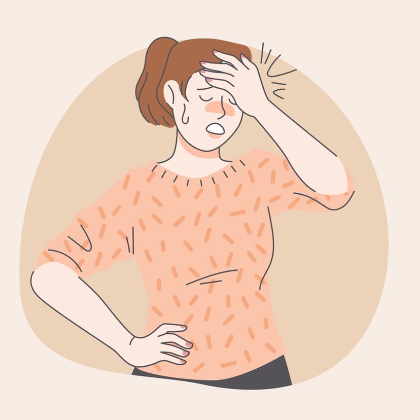 Une femme en pull orange/rosé qui a l'air de souffrir et se met sa main sur la tête.